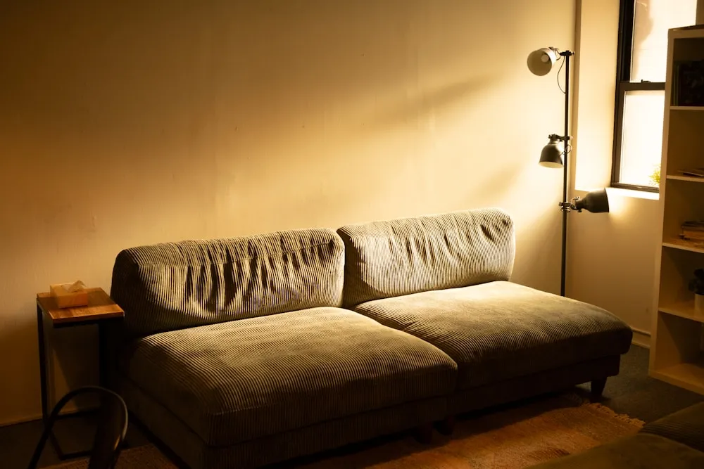Textured neutral sofa beside a wooden side table and floor lamp in warm golden light.