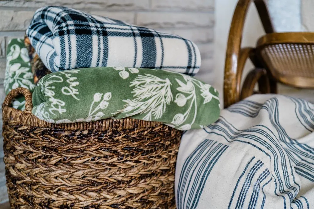 Green and blue patterned blankets folded in a woven basket beside a chair.
