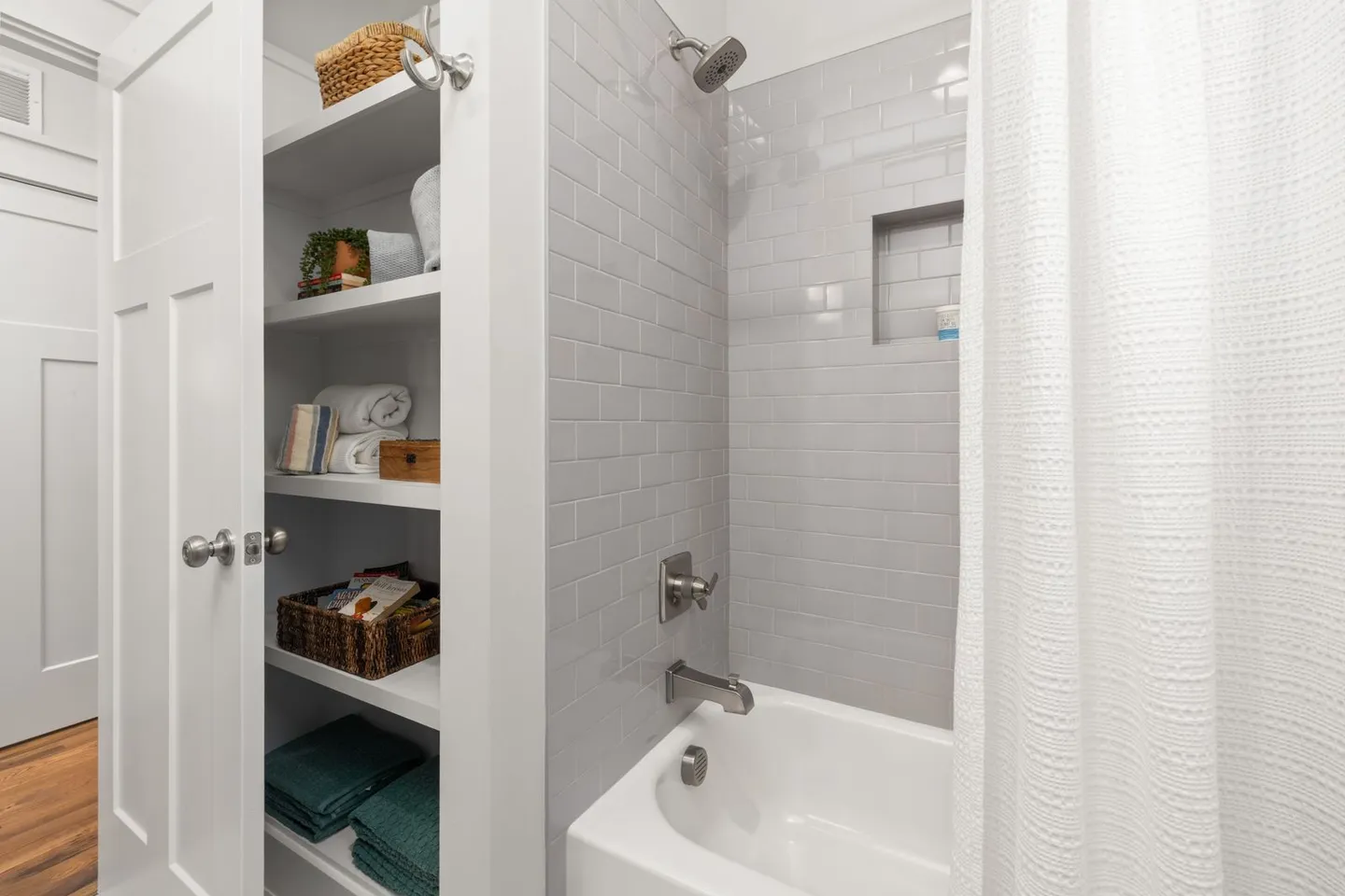 Built-in bathroom shelves holding folded towels and baskets beside a white tiled bathtub.