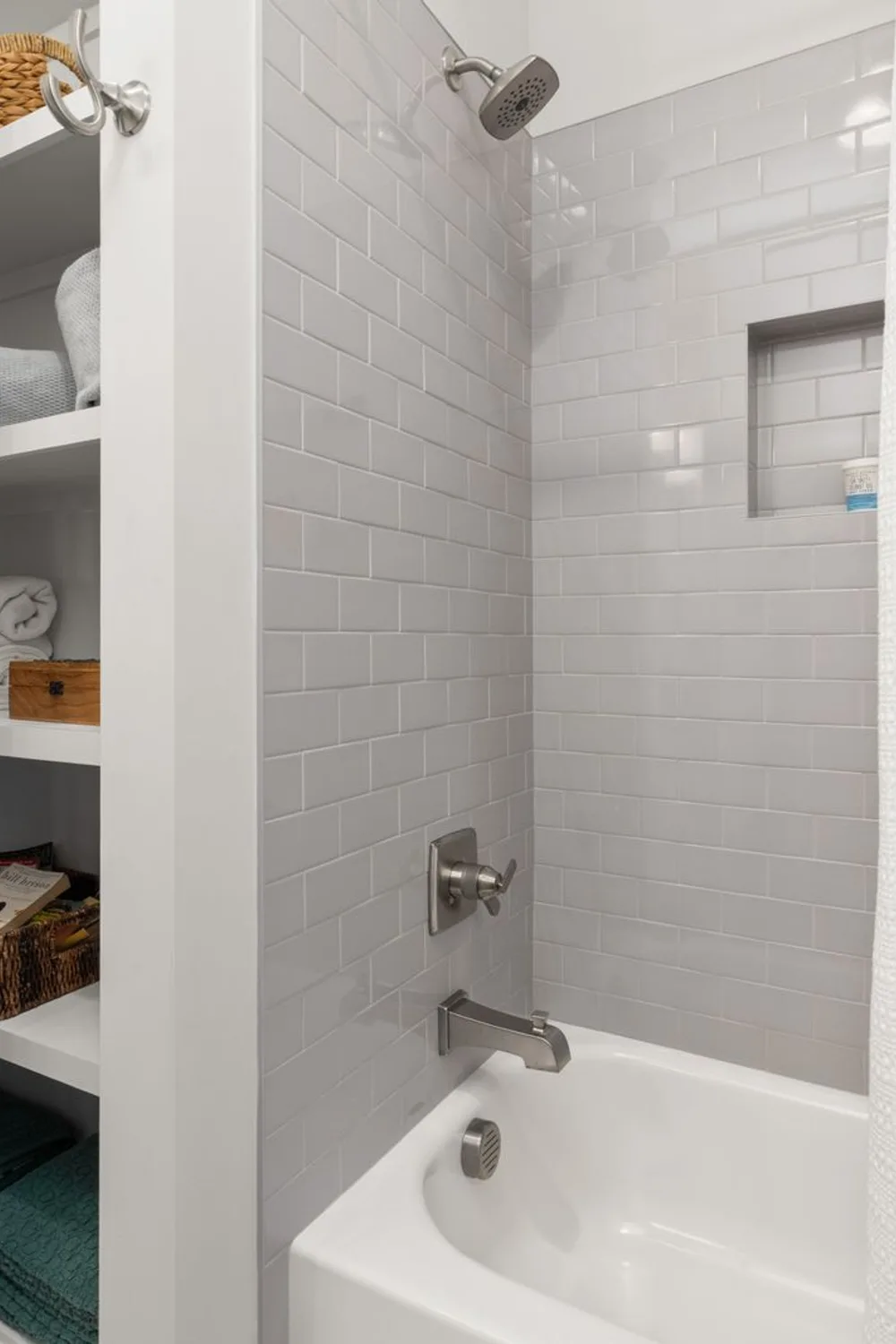 Built-in bathroom shelves holding folded towels and baskets beside a white tiled bathtub.