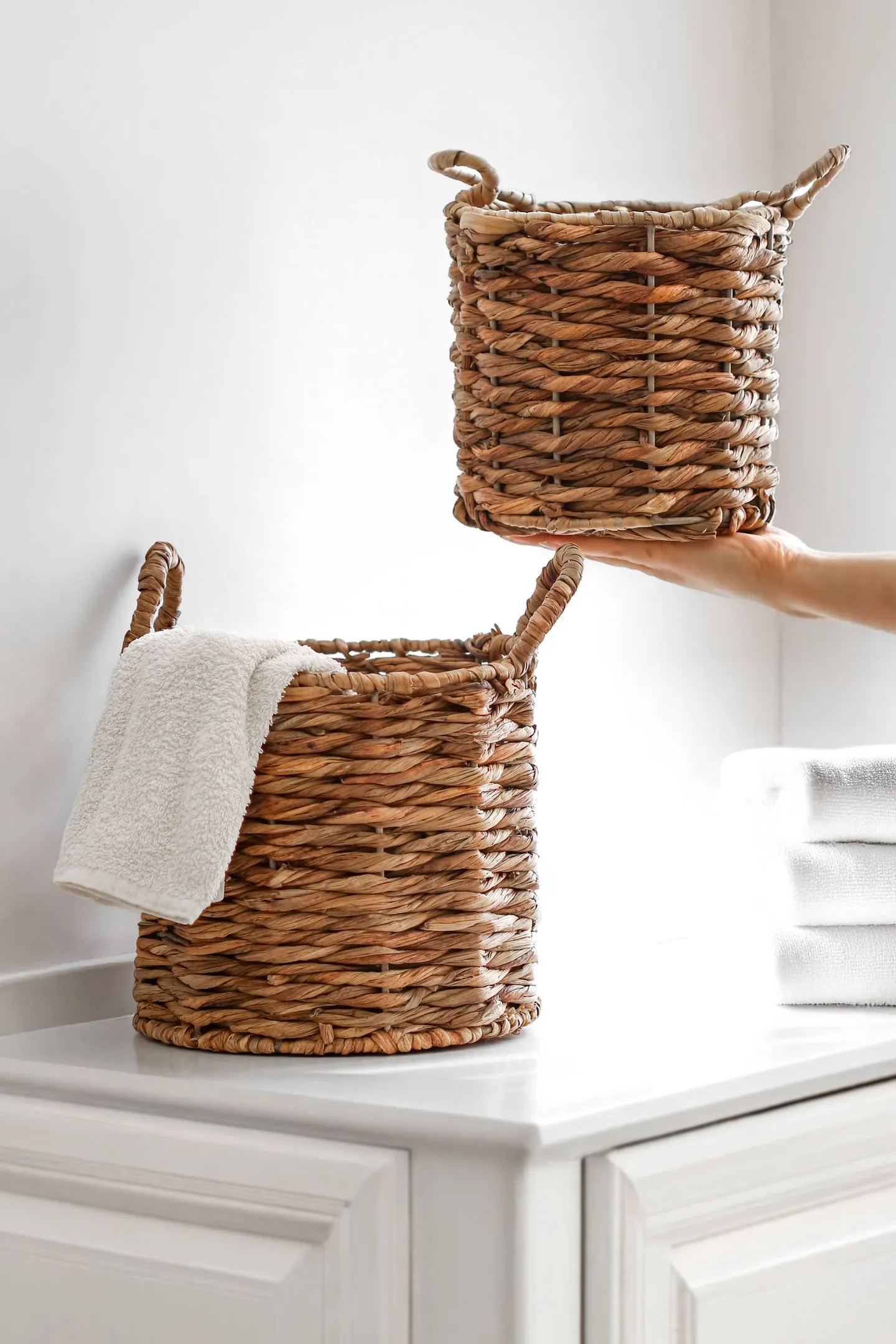 Two woven baskets with white towels on a bathroom cabinet.